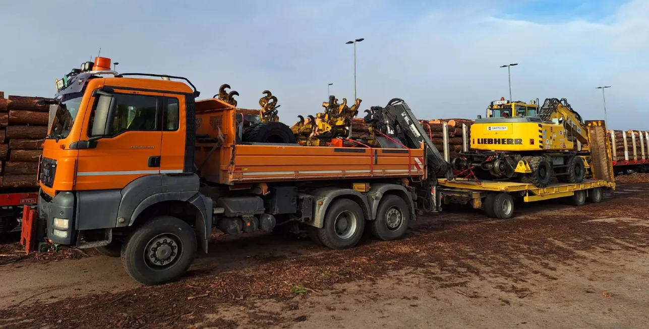 MAN LKW-Kipper und Tieflader mit Bagger auf Materialplatz